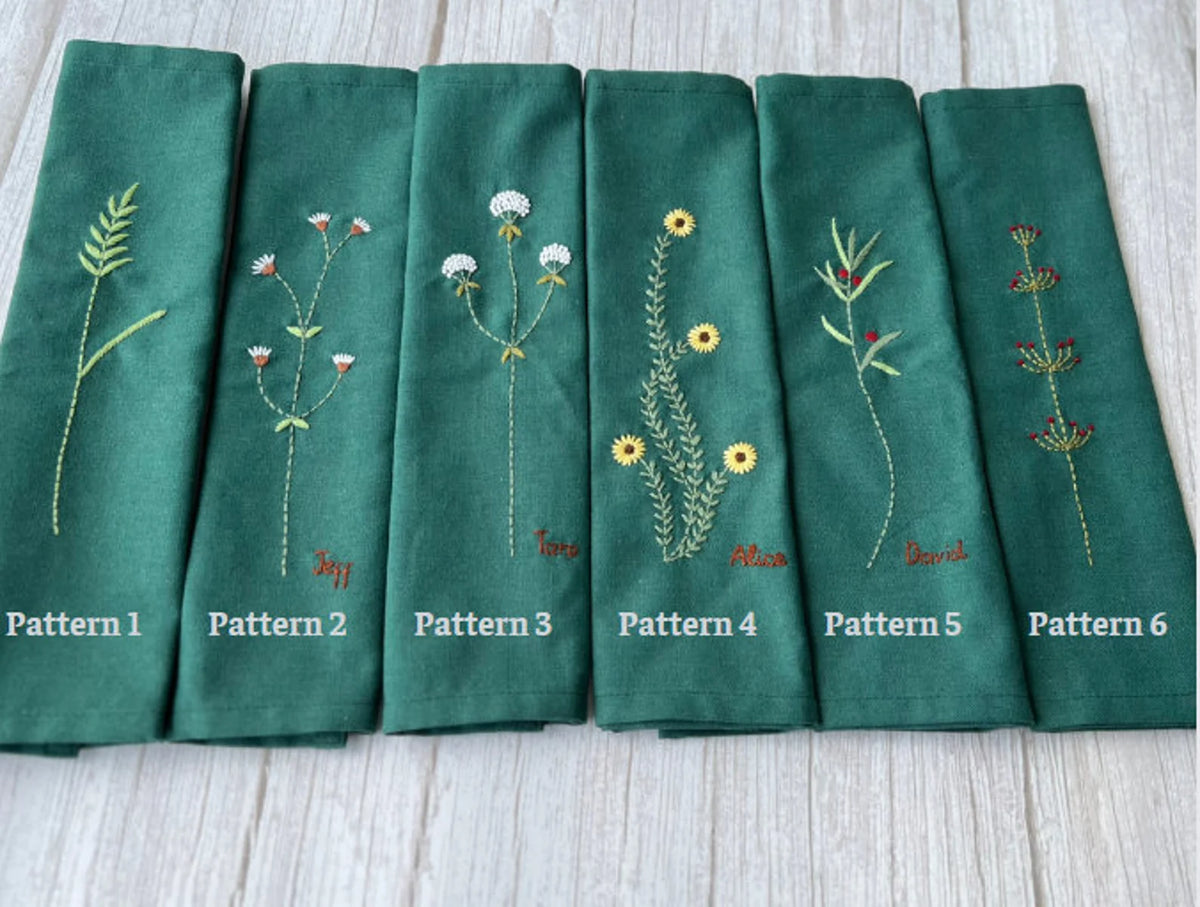 Six green linen tea towels with embroidered floral patterns and names — hand-embroidered by The Thread Nest