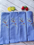 Set of four blue linen napkins with embroidered green sprigs and red berries — hand-embroidered by The Thread Nest
