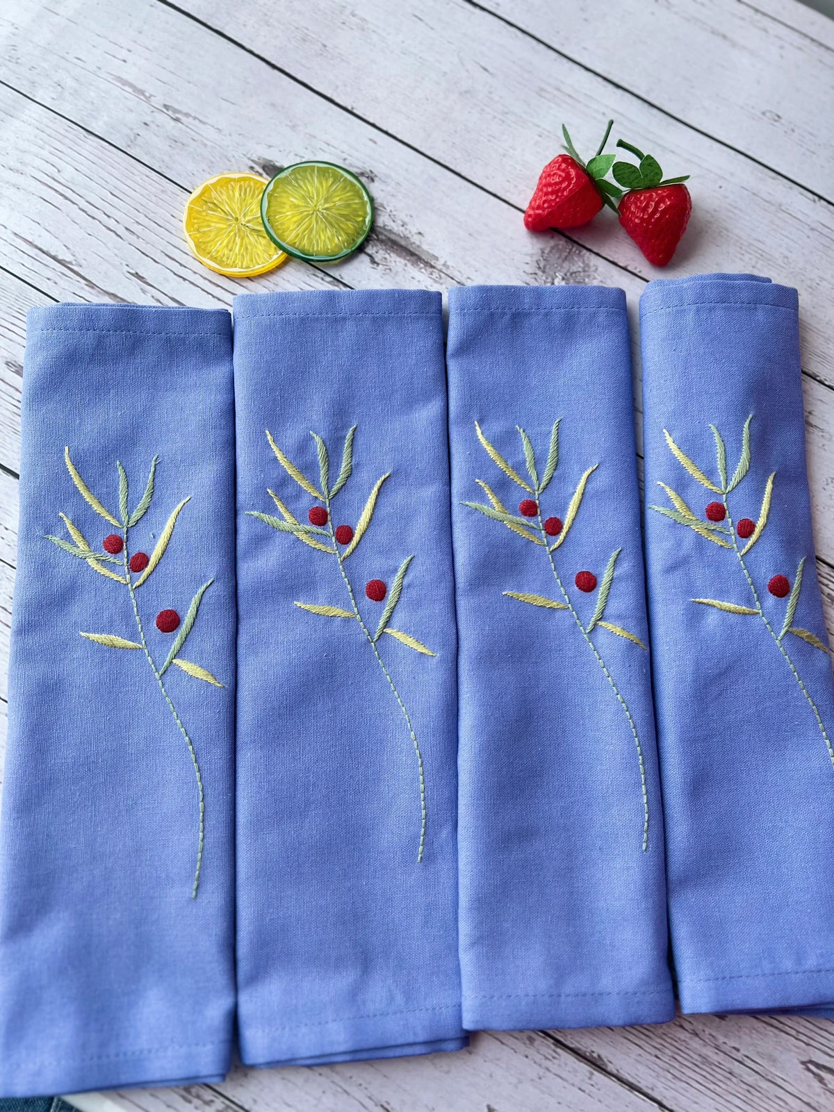 Set of four blue linen napkins with embroidered green sprigs and red berries — hand-embroidered by The Thread Nest