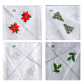 Four white linen napkins, each with a different embroidered Christmas design — hand-embroidered by The Thread Nest