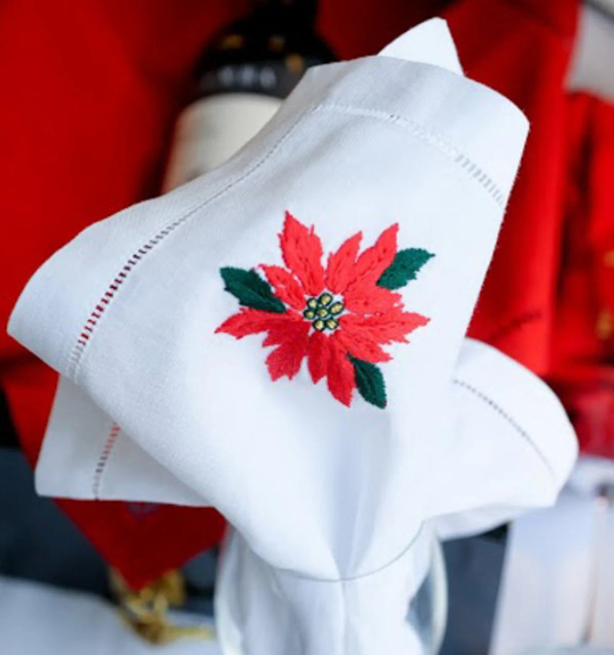 A white linen napkin with a red poinsettia embroidered on it — hand-embroidered by The Thread Nest