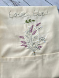 Close-up of a cream linen apron embroidered with lavender and the words Love, Liz — hand-embroidered by The Thread Nest
