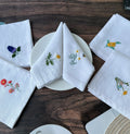 Five white linen napkins with embroidered floral designs — hand-embroidered by The Thread Nest