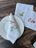 Three white linen napkins with embroidered floral designs — hand-embroidered by The Thread Nest