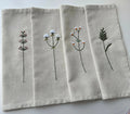 Set of four beige linen napkins with embroidered floral designs — hand-embroidered by The Thread Nest