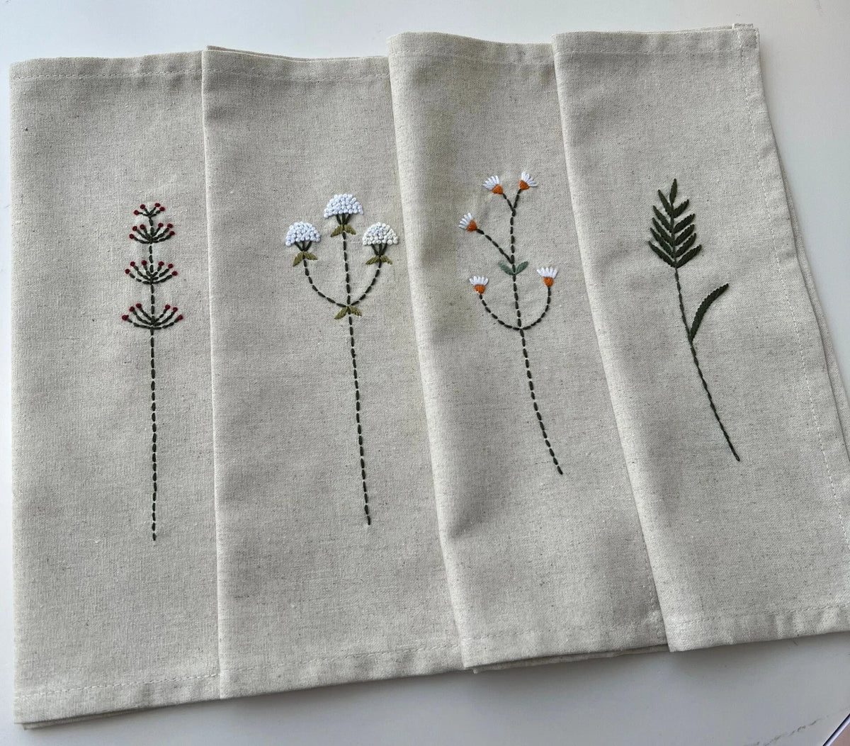Set of four beige linen napkins with embroidered floral designs — hand-embroidered by The Thread Nest