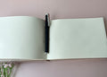 An open guest book with blank cream pages and a pen