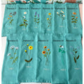 A set of seventeen teal blue linen tea towels with embroidered floral designs — hand-embroidered by The Thread Nest