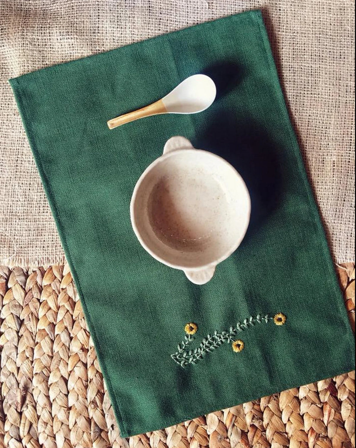 A green linen placemat with embroidered yellow flowers and leaves — hand-embroidered by The Thread Nest