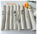 Eight embroidered linen placemats, each with a different floral design — hand-embroidered by The Thread Nest