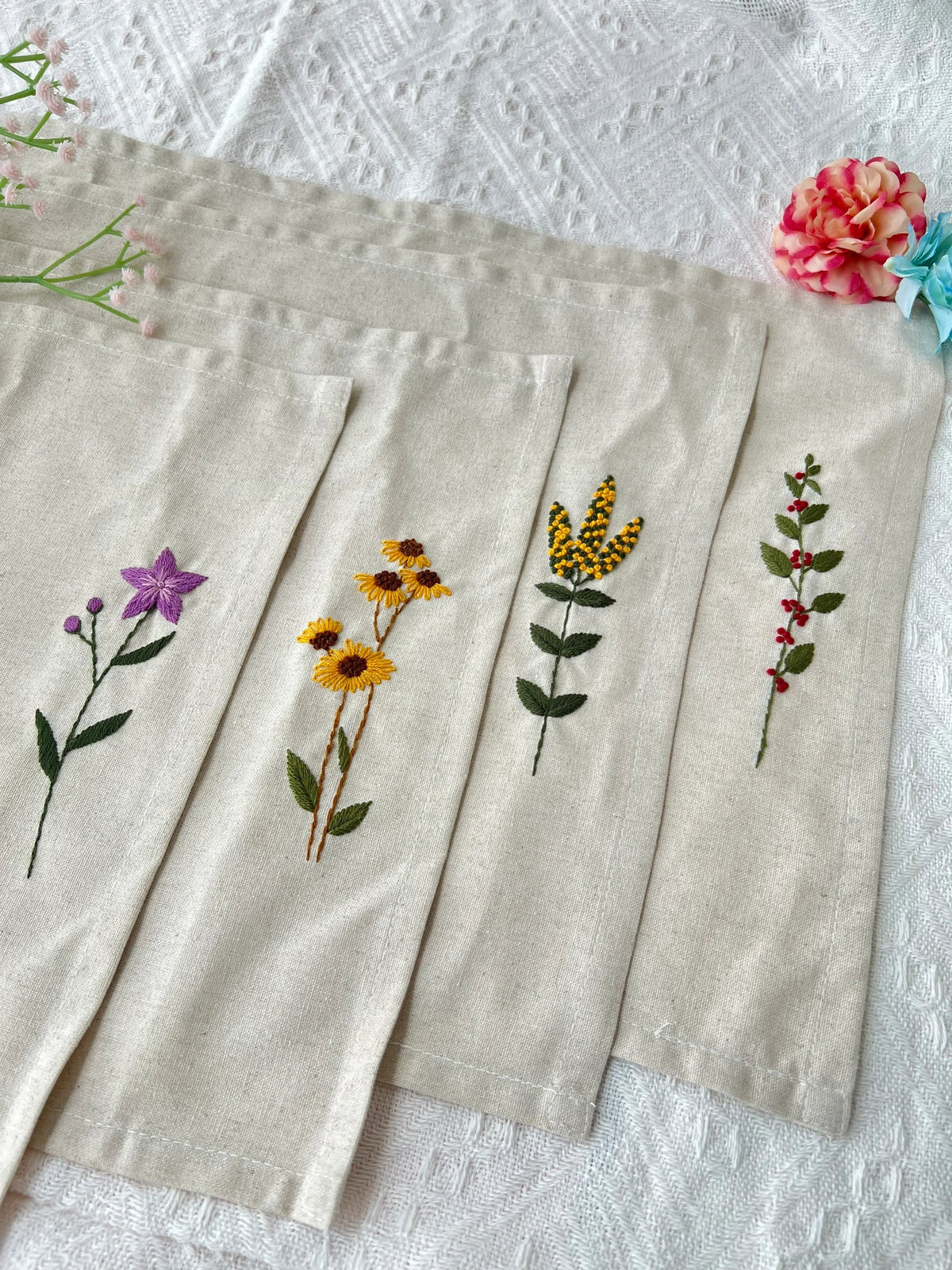 Five beige linen napkins with embroidered floral designs — hand-embroidered by The Thread Nest