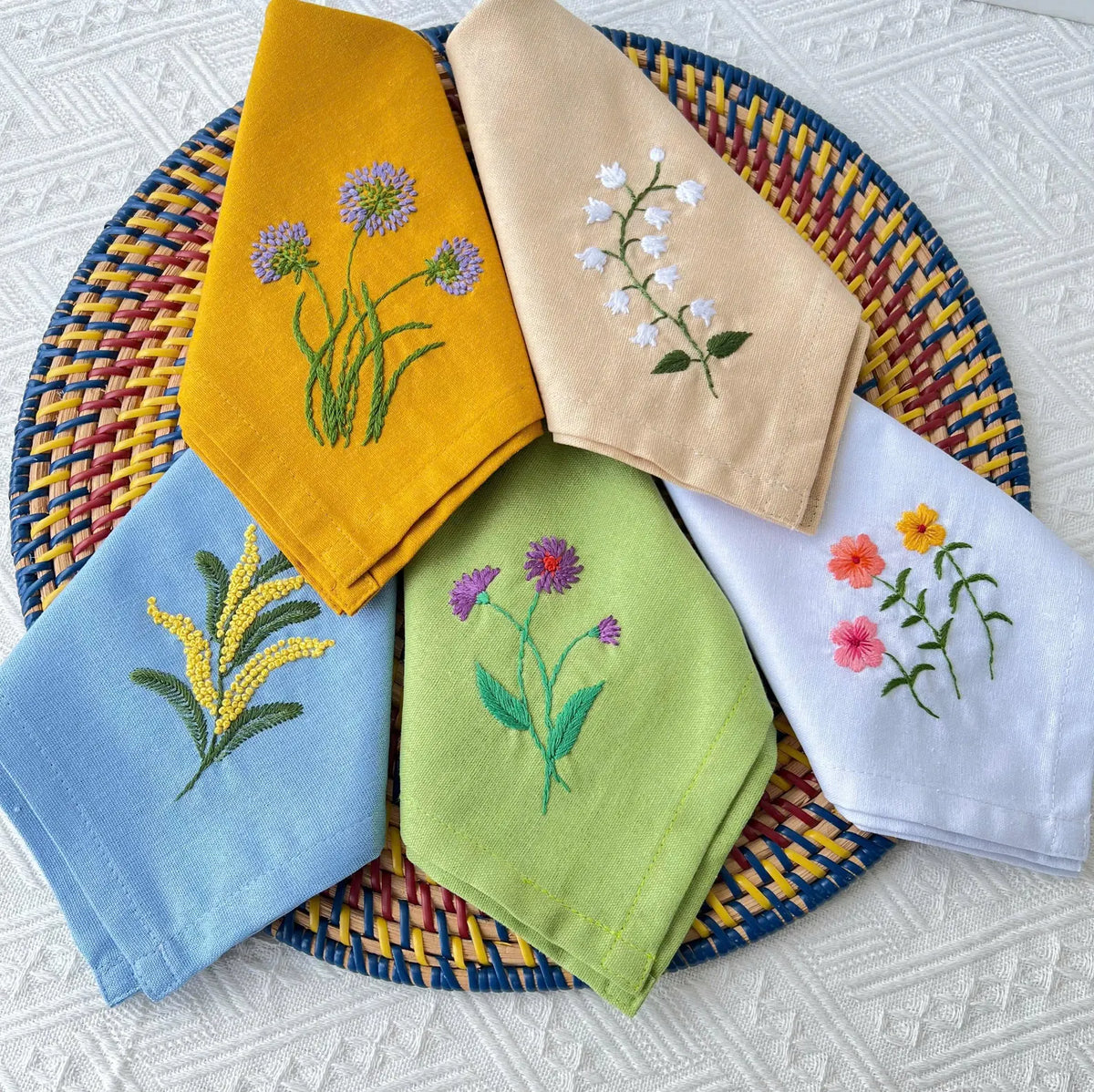 Five embroidered linen napkins, each with a different floral design — hand-embroidered by The Thread Nest