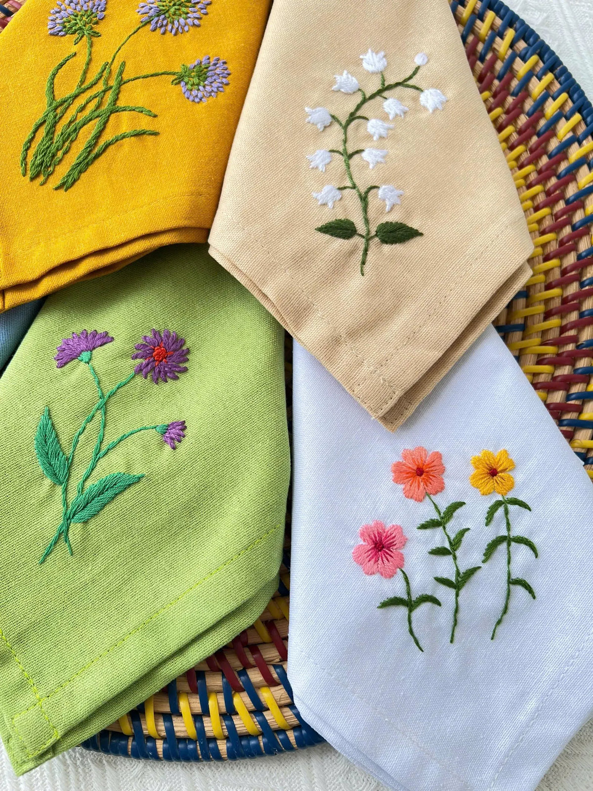 Four embroidered linen napkins, each with a different floral design — hand-embroidered by The Thread Nest