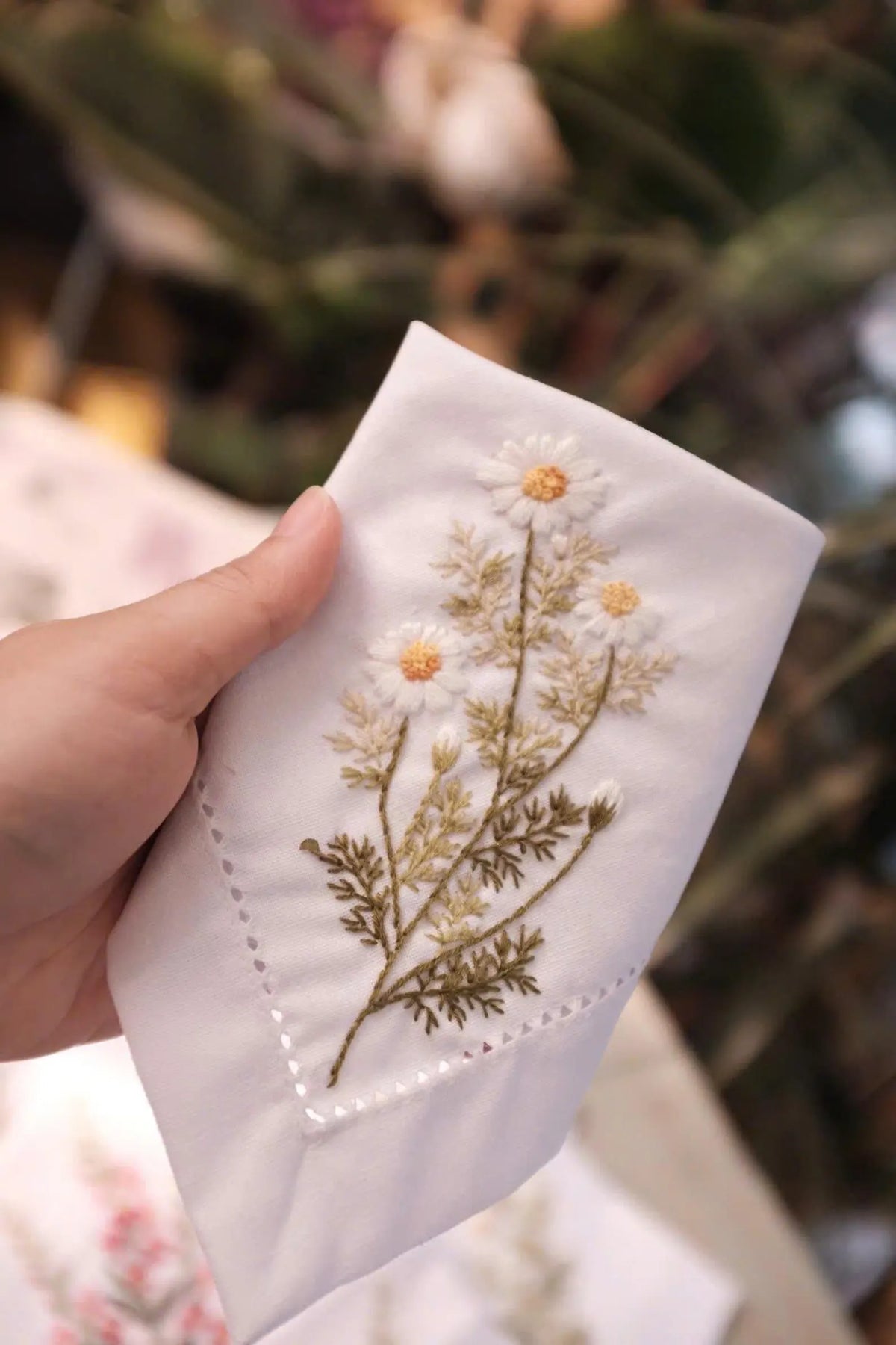 A white linen handkerchief with embroidered daisies — hand-embroidered by The Thread Nest