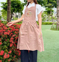 A woman wearing a pink embroidered linen apron in a garden — hand-embroidered by The Thread Nest