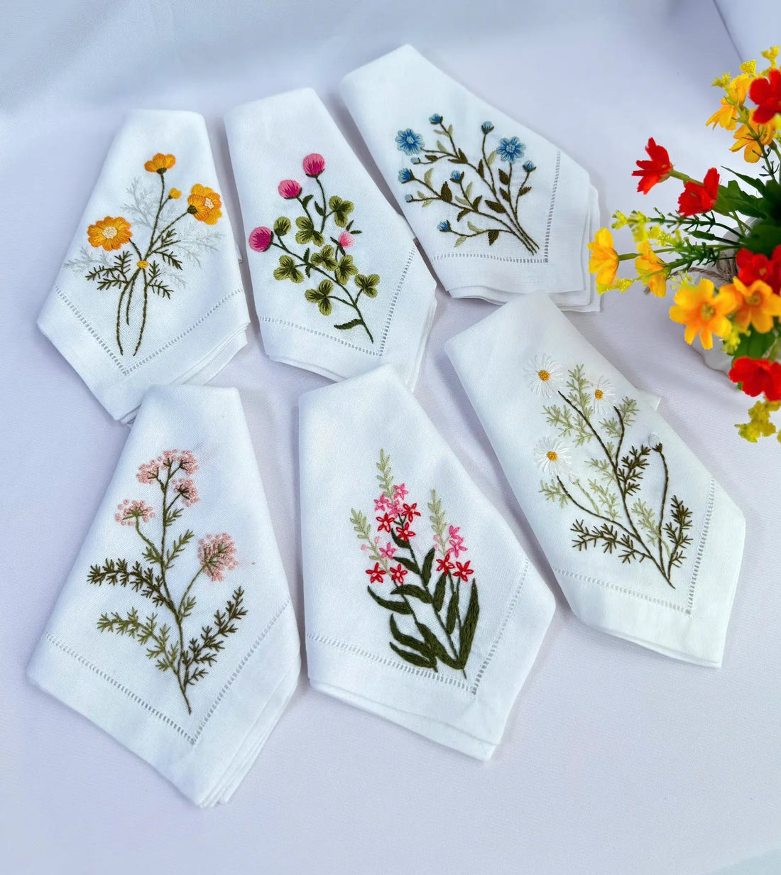 White linen napkins with embroidered floral designs — hand-embroidered by The Thread Nest