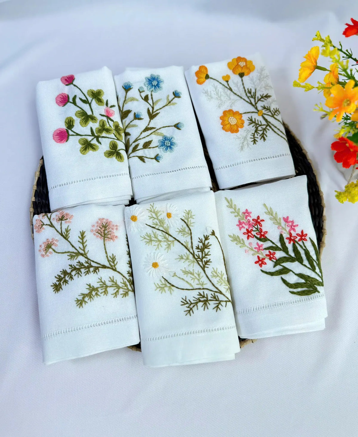 A collection of white embroidered linen hand towels, each with a different floral design — hand-embroidered by The Thread Nest
