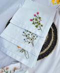 White linen napkins with embroidered floral designs — hand-embroidered by The Thread Nest