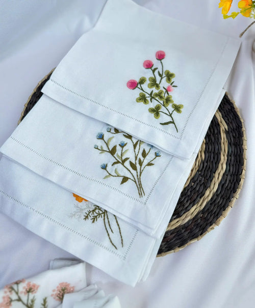 White linen napkins with embroidered floral designs — hand-embroidered by The Thread Nest