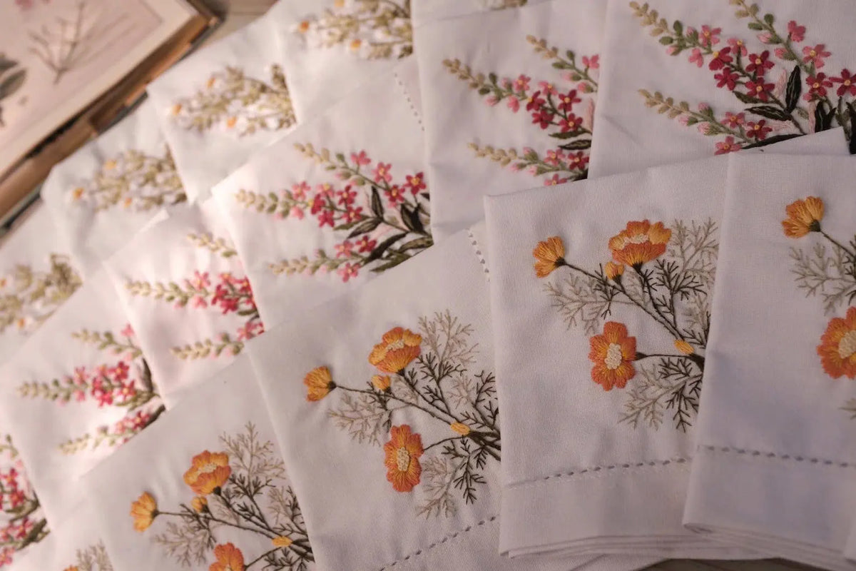 White linen napkins with embroidered floral designs in orange, pink and yellow — hand-embroidered by The Thread Nest