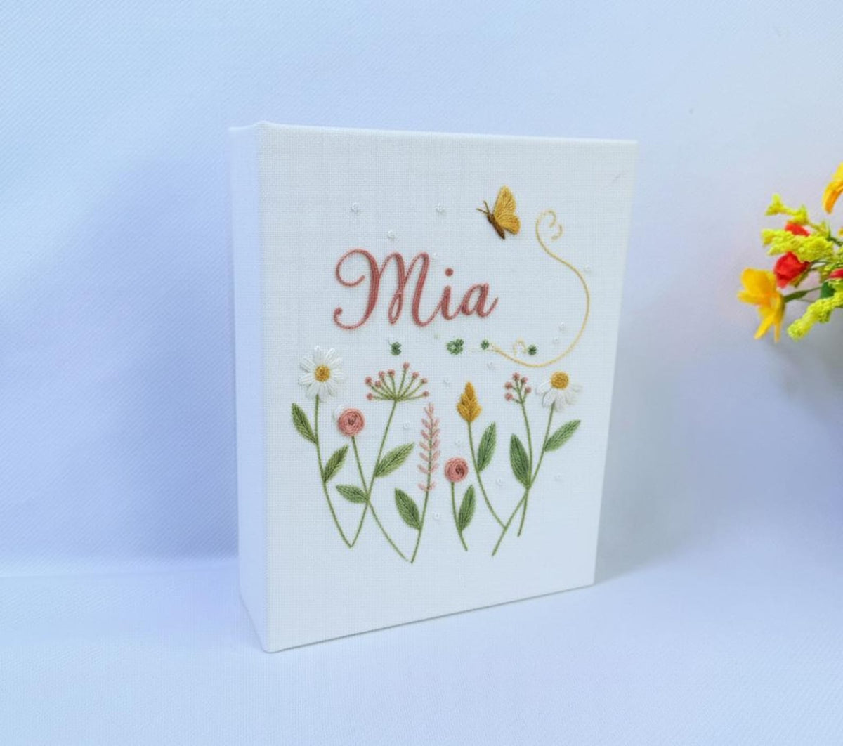A white keepsake box with embroidered flowers in green, pink, yellow and white — hand-embroidered by The Thread Nest