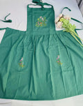 A green linen kids apron with embroidered wildflowers on the bib and pockets — hand-embroidered by The Thread Nest