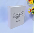 A light gray photo album with line art of two birds holding heart-shaped pendants — hand-embroidered by The Thread Nest