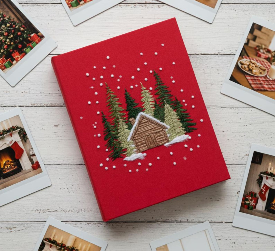 A beige book with an embroidered winter scene of a cabin and pine trees — hand-embroidered by The Thread Nest