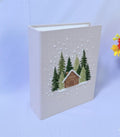 A beige book with an embroidered winter scene of a cabin and pine trees — hand-embroidered by The Thread Nest