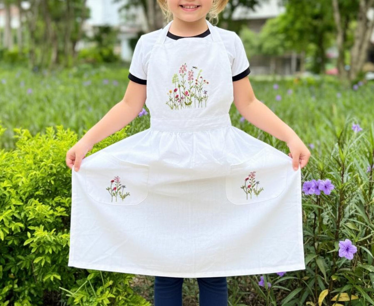 A child holding out a white linen kids apron embroidered with wildflowers — hand-embroidered by The Thread Nest