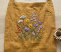 Close-up of the embroidered wildflower bouquet on a mustard linen apron — hand-embroidered by The Thread Nest