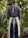 Back view of a woman wearing a beige linen apron tied in a bow — hand-embroidered by The Thread Nest