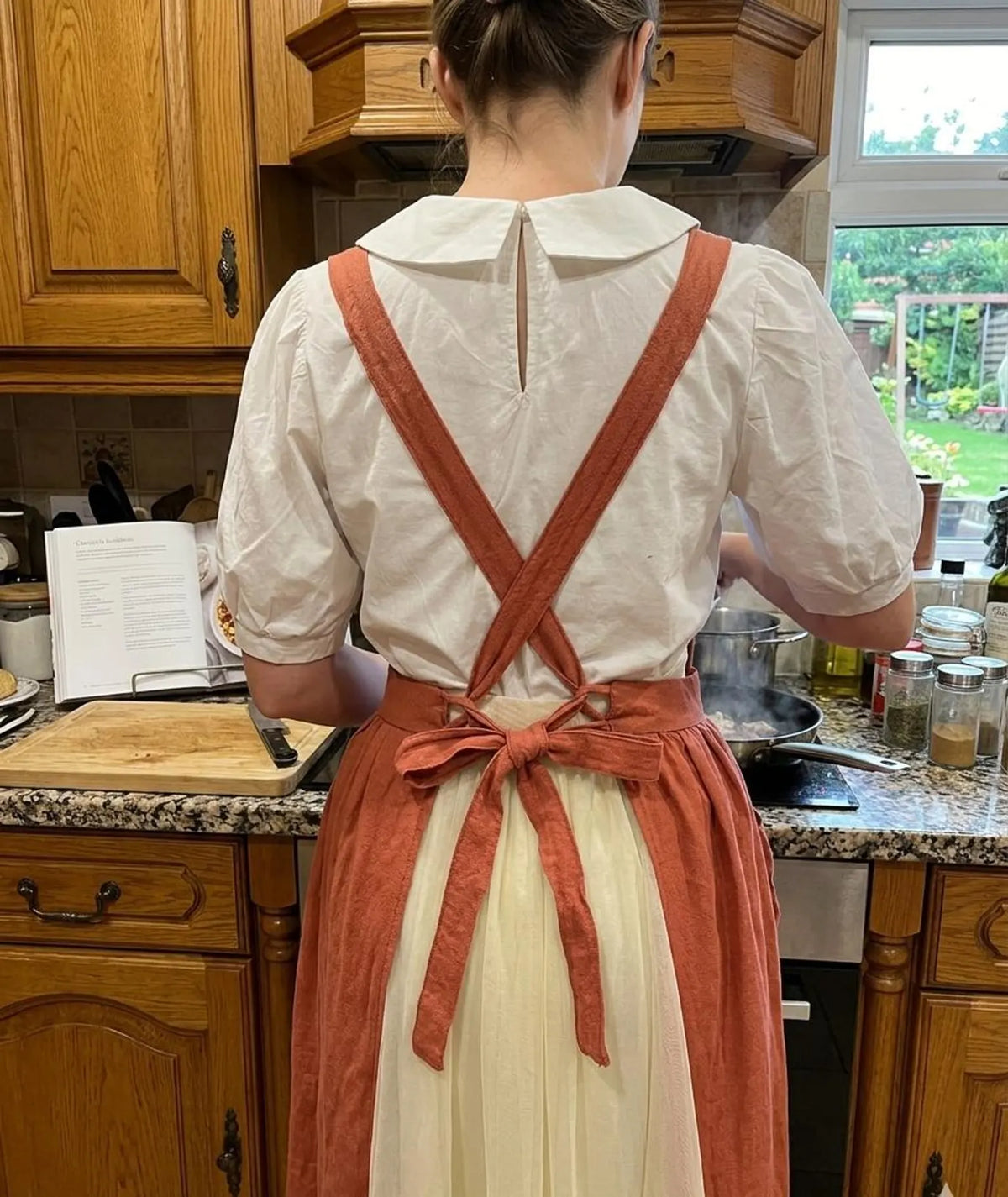 Back view of a woman wearing a rust ruffled apron with crossed straps tied in a bow — hand-embroidered by The Thread Nest