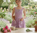 A woman wearing a lavender ruffled linen apron in a garden — hand-embroidered by The Thread Nest