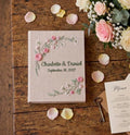 A beige linen guest book with embroidered pink roses and green foliage — hand-embroidered by The Thread Nest