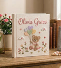 A cream-colored photo album with a brown teddy bear in a pink bow — hand-embroidered by The Thread Nest