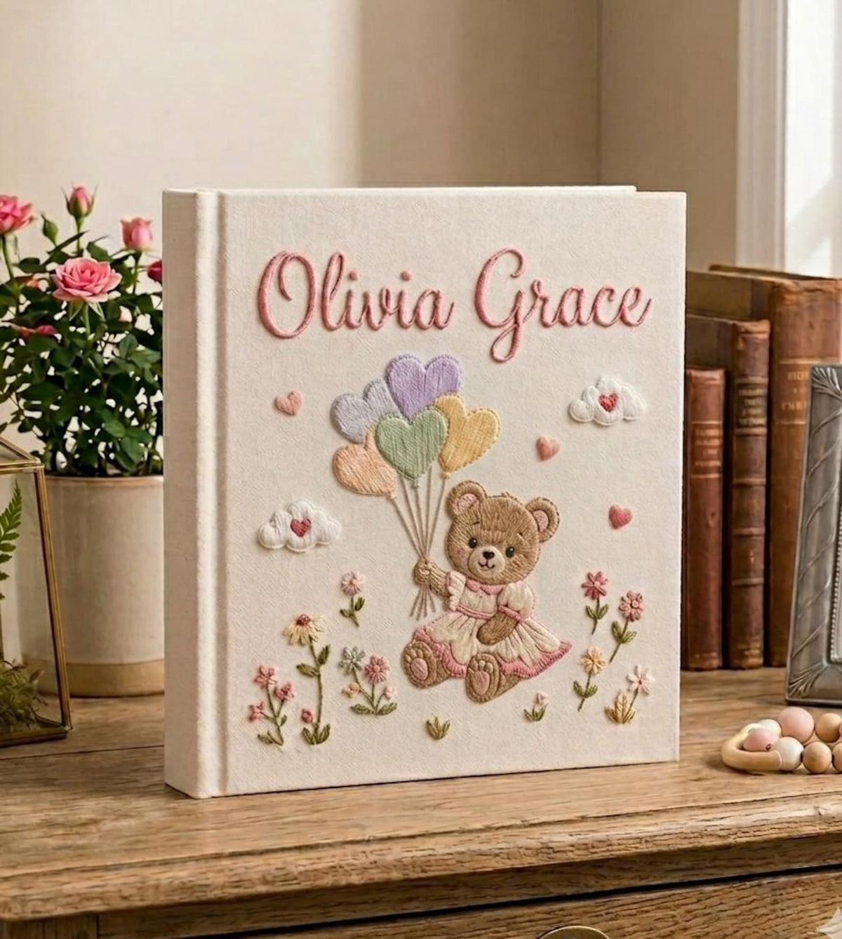 A cream-colored photo album with a brown teddy bear in a pink bow — hand-embroidered by The Thread Nest