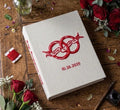 An off-white book with red embroidered interlocking rings and a ribbon banner — hand-embroidered by The Thread Nest
