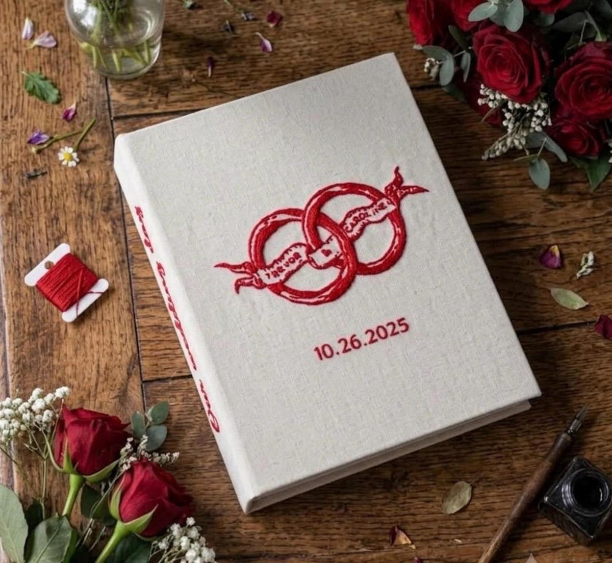 An off-white book with red embroidered interlocking rings and a ribbon banner — hand-embroidered by The Thread Nest