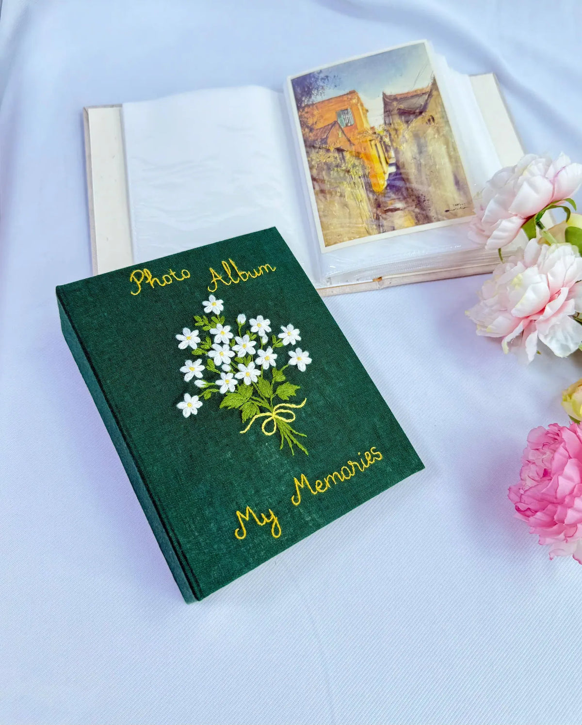 A dark green photo album with embroidered white flowers and gold lettering — hand-embroidered by The Thread Nest