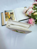 An open photo album showing a watercolour painting of a street scene — hand-embroidered by The Thread Nest