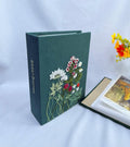 A dark green fabric-covered photo album with an embroidered floral design in white, red and green — hand-embroidered by The Thread Nest