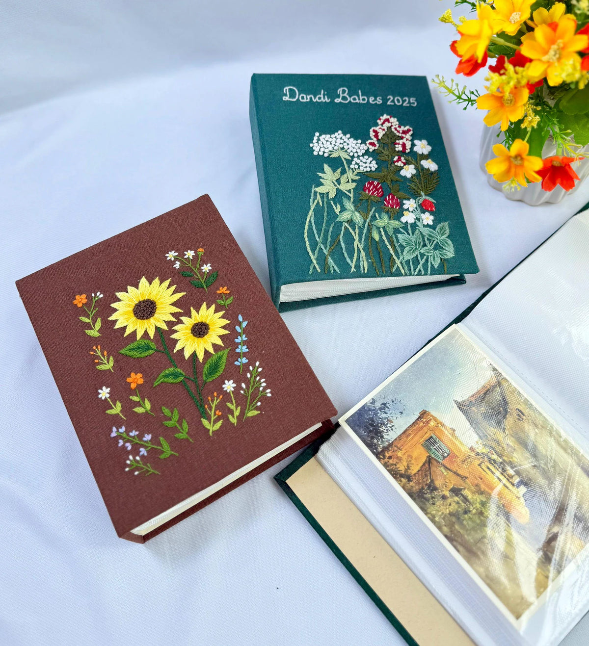 Two fabric-covered photo albums with embroidered floral designs — hand-embroidered by The Thread Nest