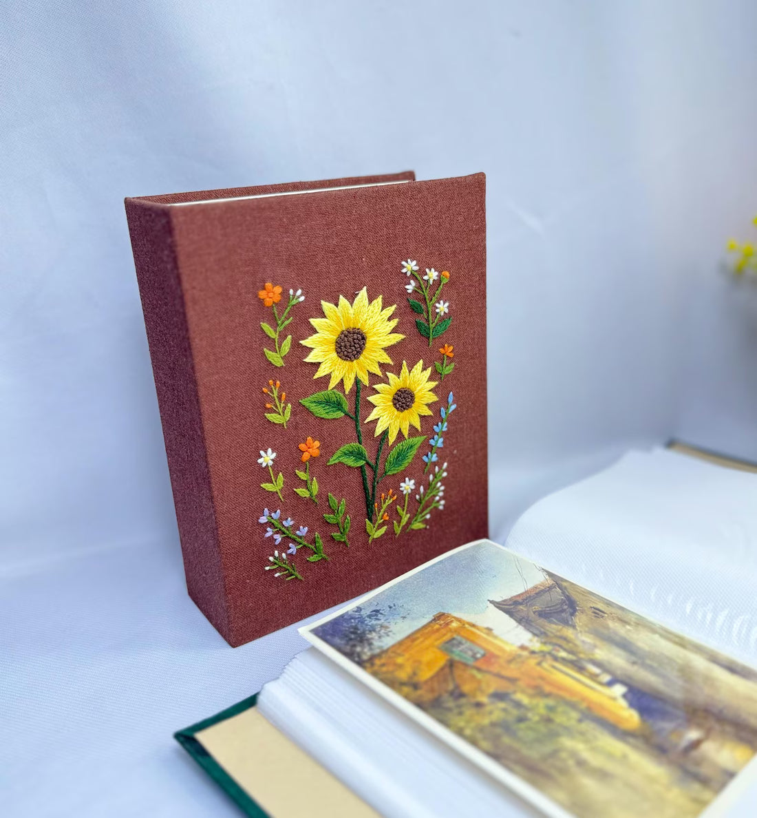 A dark green fabric-covered photo album with an embroidered floral design in white, red and green — hand-embroidered by The Thread Nest