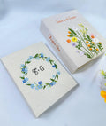 Two beige embroidered books with floral designs and stitched text — hand-embroidered by The Thread Nest
