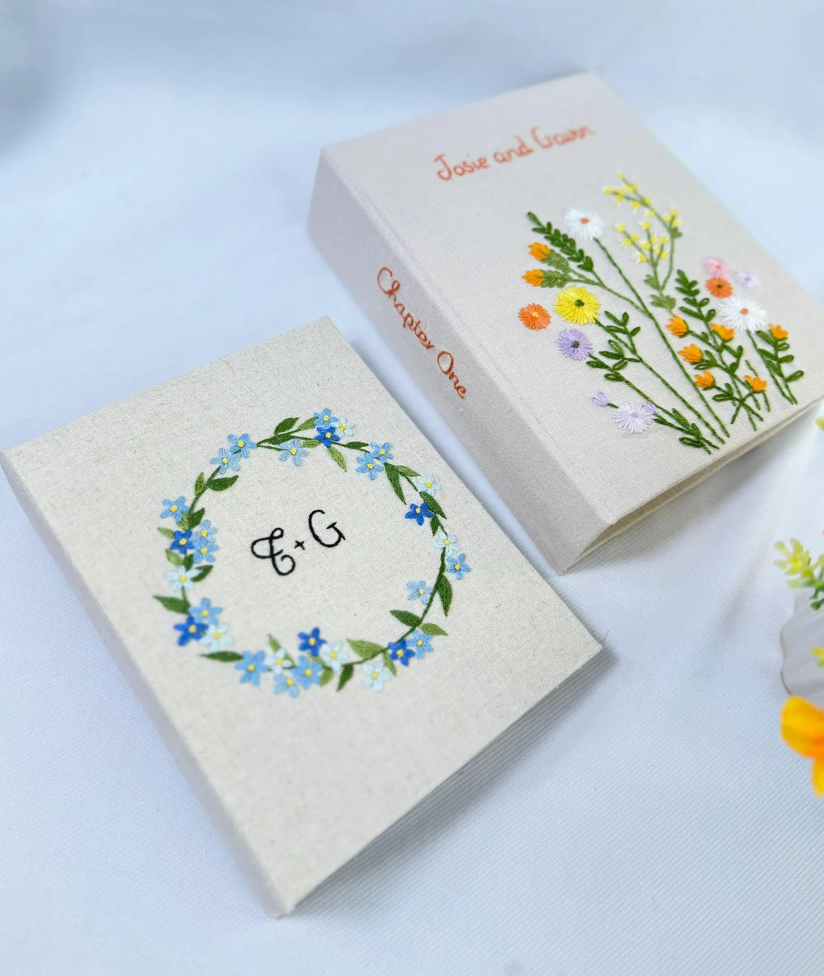 Two beige embroidered books with floral designs and stitched text — hand-embroidered by The Thread Nest