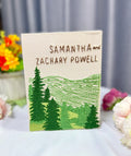 An embroidered canvas of a forest scene with green trees and rolling hills — hand-embroidered by The Thread Nest