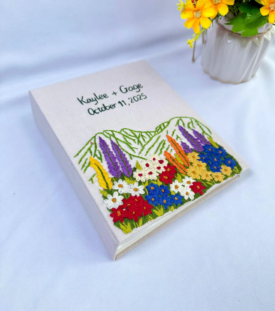 A cream-colored cover with embroidered names, a date and a colourful floral design — hand-embroidered by The Thread Nest