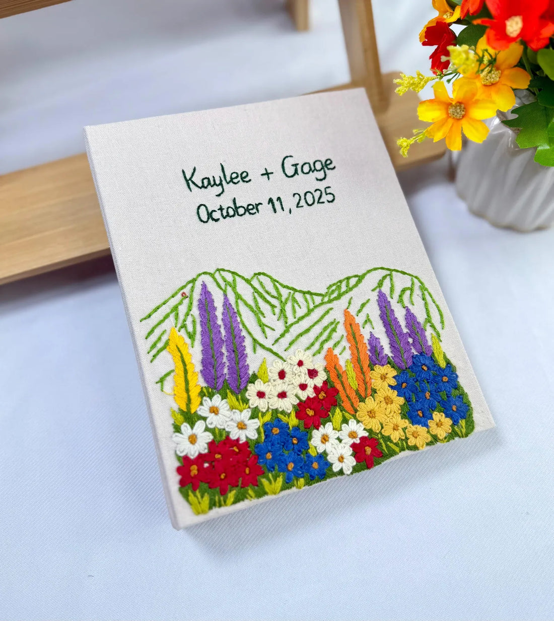 A cream-colored cover with embroidered names, a date and a colourful floral design — hand-embroidered by The Thread Nest