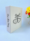 A cream-colored photo album with black embroidered hearts and Our Love Story on the spine — hand-embroidered by The Thread Nest